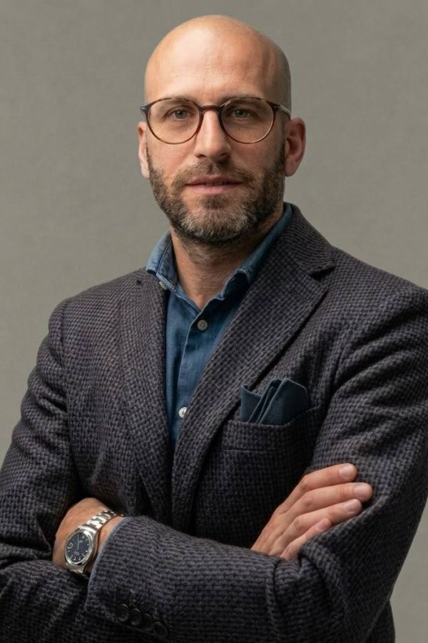 Foto a mezzo busto professionale di Carlo Apostoli con giacca grigia, camicia blu, sfondo grigio